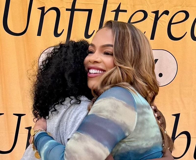 Two women hugging with a 'Unfiltered' background